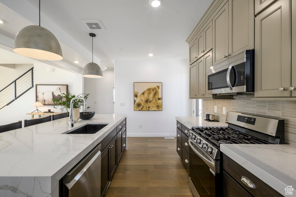Kitchen featuring baseboards, dark wood-style floors, tasteful backsplash, a sink, and appliances with stainless steel finishes