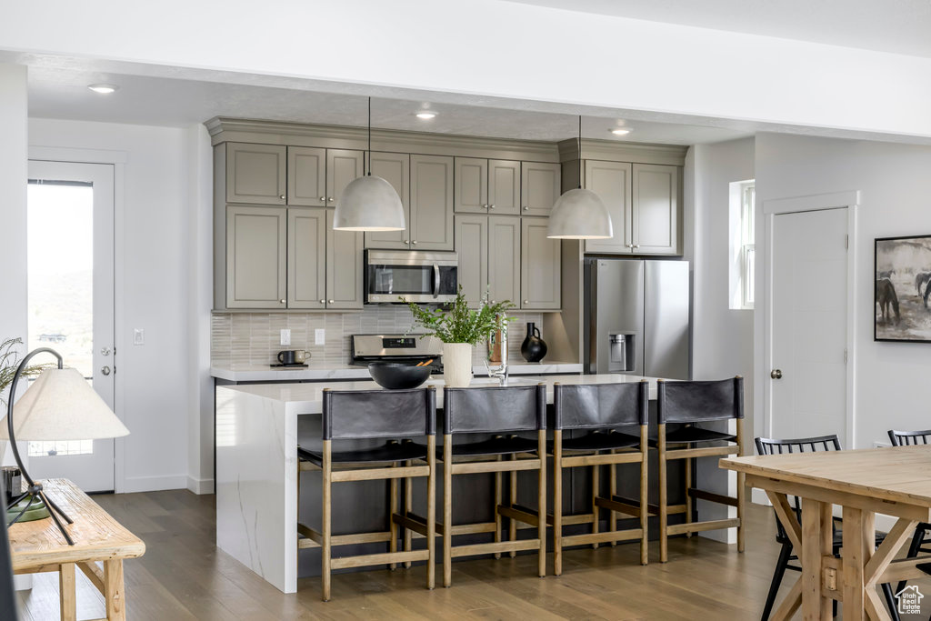 Kitchen with an island with sink, light countertops, dark wood finished floors, appliances with stainless steel finishes, and gray cabinetry