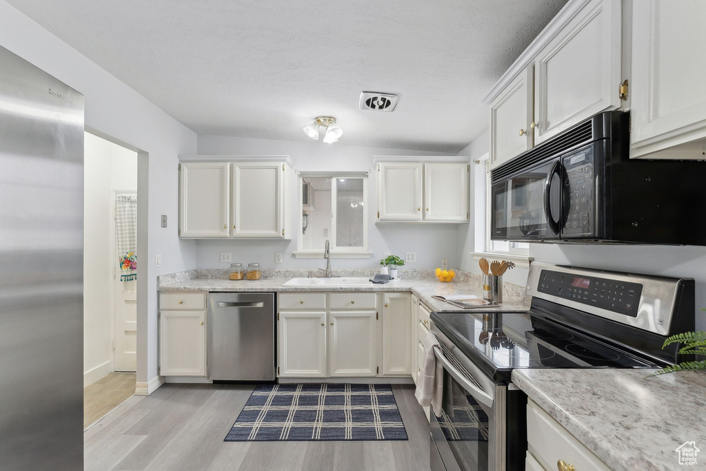 Kitchen with white cabinets, sink, light wood-type flooring, and stainless steel appliances