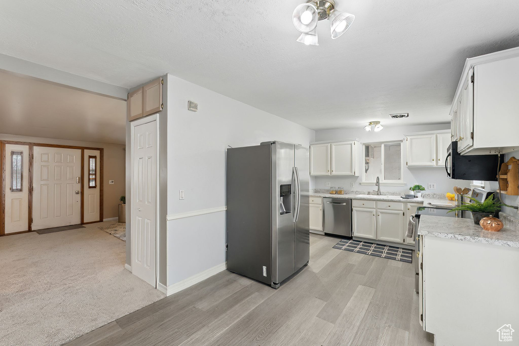 Kitchen with appliances with stainless steel finishes, ceiling fan, sink, white cabinets, and light hardwood / wood-style floors