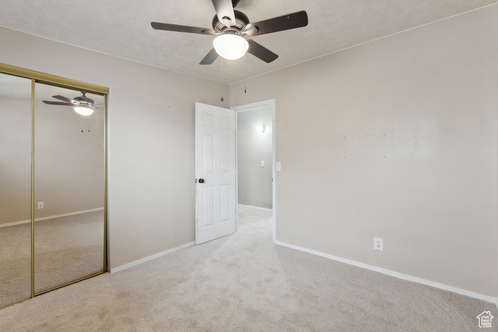 Unfurnished bedroom featuring ceiling fan, a closet, and light carpet