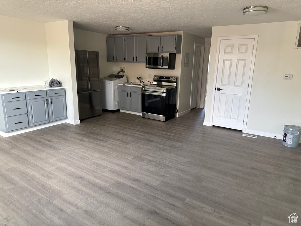 Kitchen with gray cabinetry, washer / clothes dryer, a textured ceiling, appliances with stainless steel finishes, and hardwood / wood-style flooring