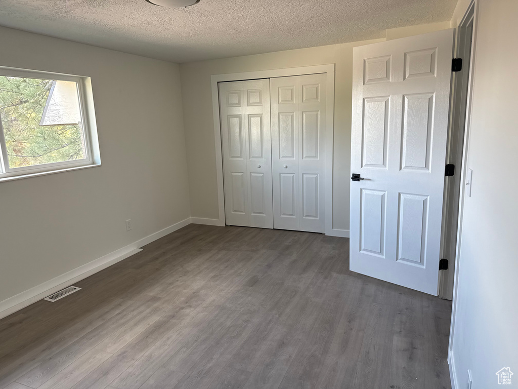 Unfurnished bedroom with a textured ceiling, dark hardwood / wood-style flooring, and a closet