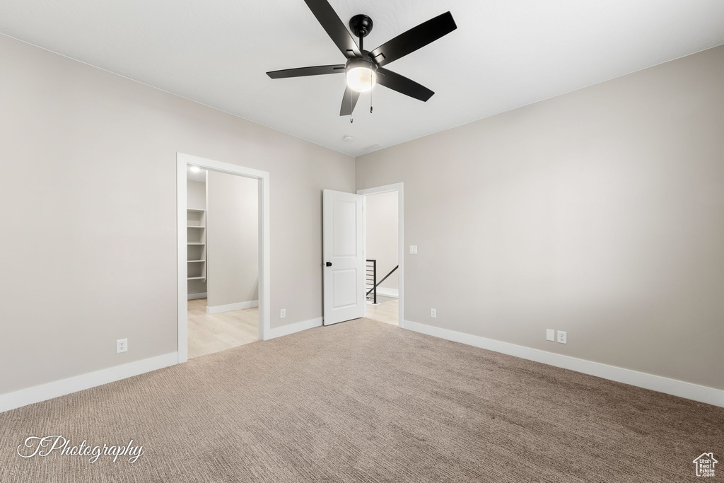 Unfurnished bedroom featuring a walk in closet, ceiling fan, a closet, and light colored carpet