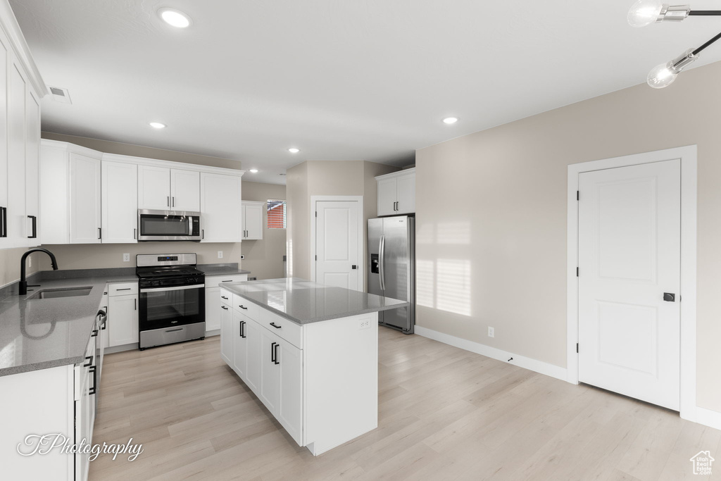 Kitchen featuring a center island, white cabinets, sink, light wood-type flooring, and stainless steel appliances