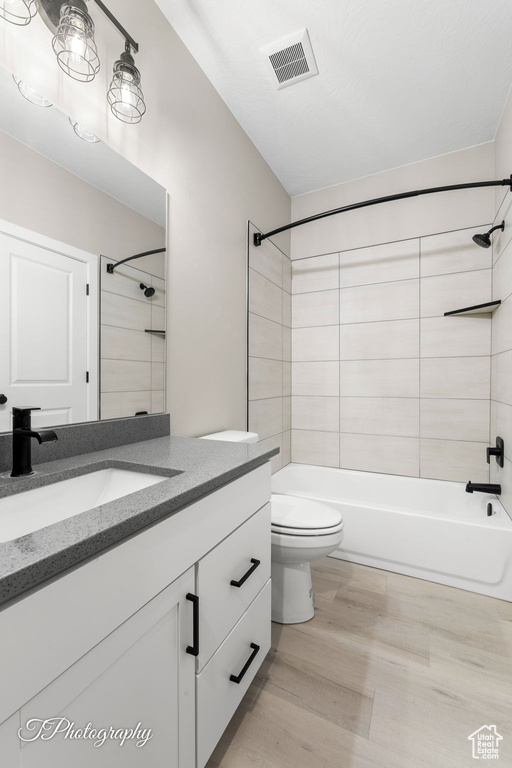 Full bathroom featuring vanity, wood-type flooring, tiled shower / bath combo, and toilet