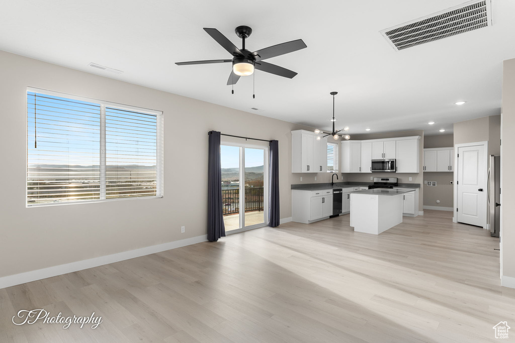 Kitchen featuring a center island, white cabinets, decorative light fixtures, light hardwood / wood-style floors, and stainless steel appliances