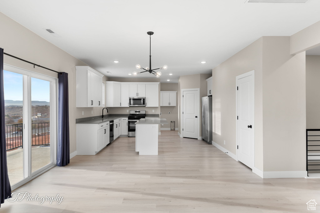 Kitchen with a kitchen island, a notable chandelier, decorative light fixtures, white cabinets, and appliances with stainless steel finishes