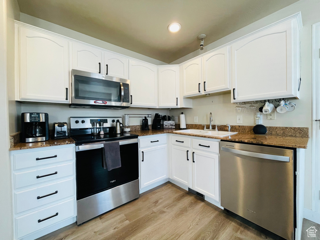 Kitchen featuring appliances with stainless steel finishes, dark stone counters, sink, light hardwood / wood-style flooring, and white cabinetry