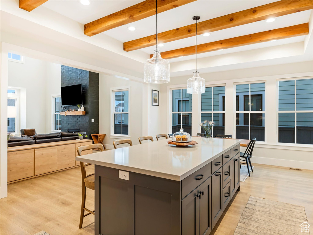 Kitchen with a center island, a kitchen breakfast bar, beam ceiling, decorative light fixtures, and light hardwood / wood-style floors