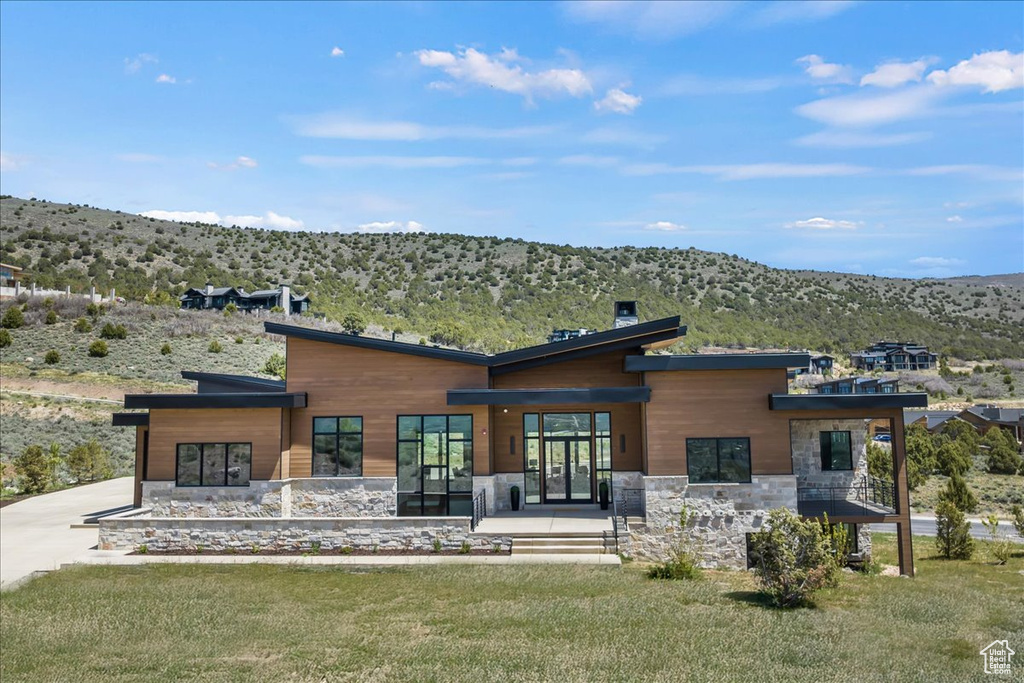 Rear view of house featuring a mountain view, stone siding, driveway, and a yard