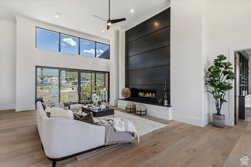 Living room featuring a towering ceiling, a fireplace, baseboards, wood finished floors, and ornamental molding