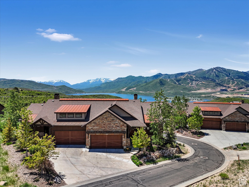 View of front of home featuring driveway, a water and mountain view, a chimney, stone siding, and roof with shingles