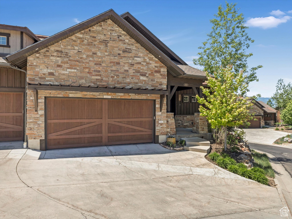 View of front facade with stone siding, driveway, and an attached garage