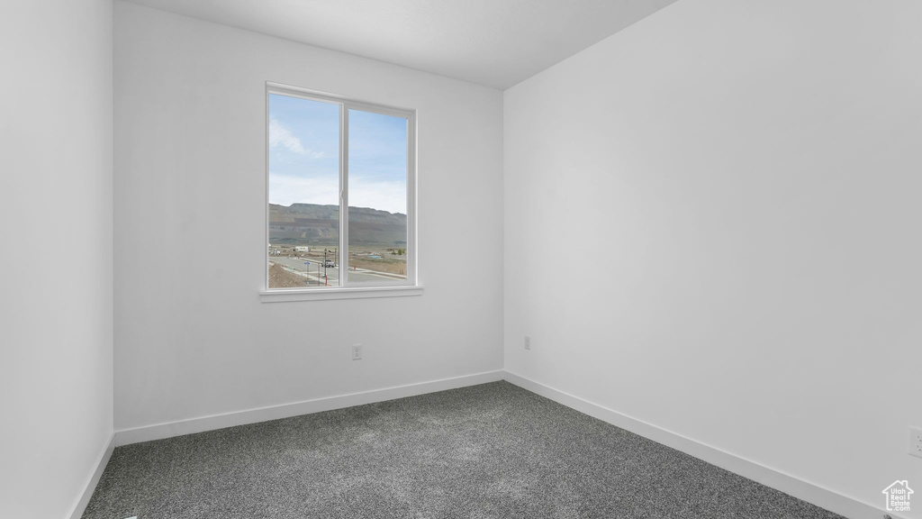 Unfurnished room featuring plenty of natural light, baseboards, and dark colored carpet