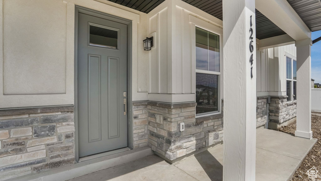 View of exterior entry with stone siding, a porch, and board and batten siding