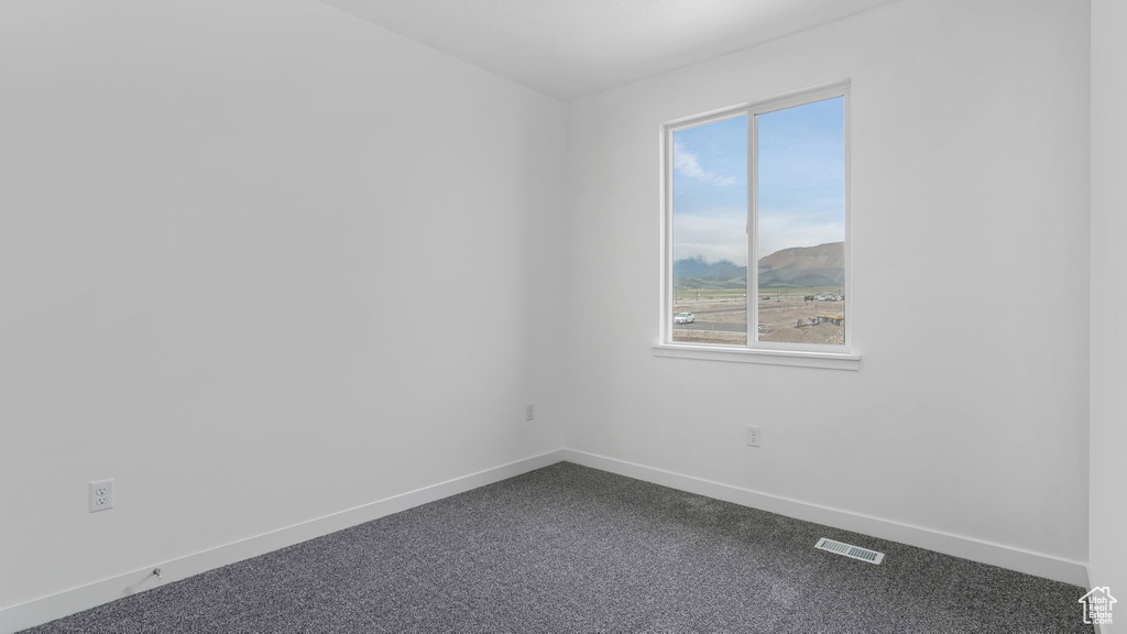 Empty room featuring dark carpet, baseboards, healthy amount of natural light, and a mountain view