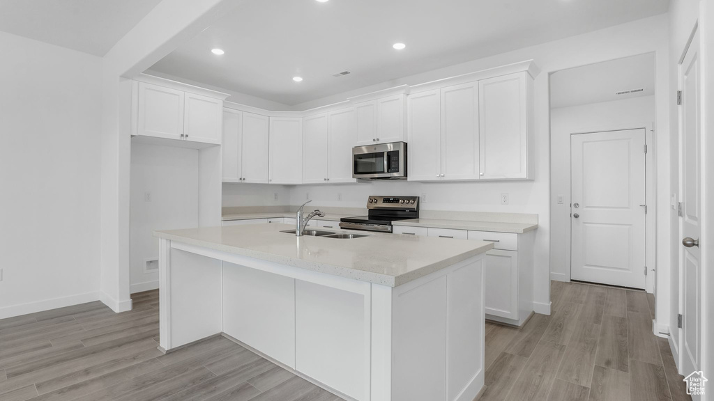 Kitchen with appliances with stainless steel finishes, a sink, light wood finished floors, white cabinets, and recessed lighting