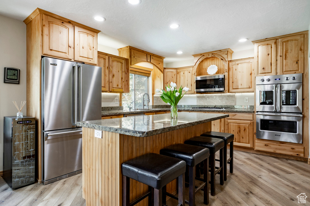 Kitchen with appliances with stainless steel finishes, light wood-style flooring, recessed lighting, dark stone counters, and a kitchen island