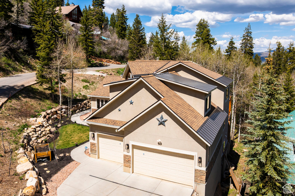 View of front of property with stucco siding, stone siding, driveway, and roof with shingles