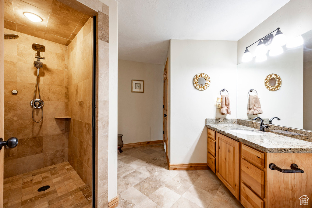 Full bath with tiled shower, vanity, and baseboards