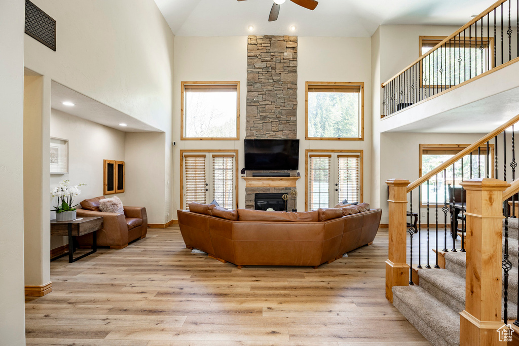 Living room with a towering ceiling, ceiling fan, a stone fireplace, stairway, and wood finished floors