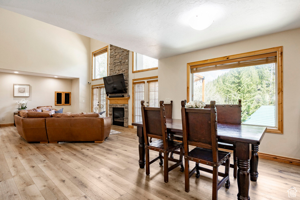 Dining space featuring light wood-style flooring, plenty of natural light, baseboards, a fireplace, and a high ceiling