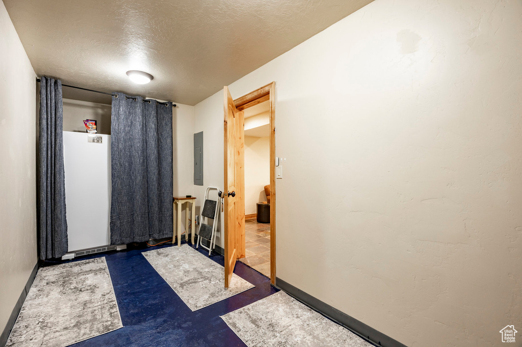 Spare room featuring a textured ceiling, electric panel, finished concrete floors, and baseboards