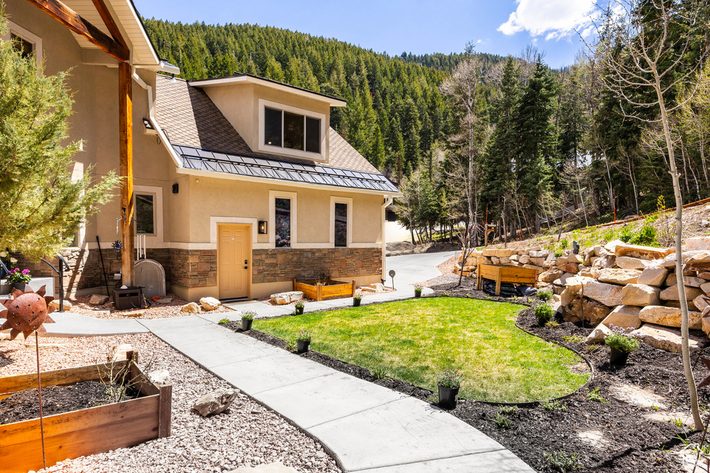 Back of property with a wooded view, stucco siding, stone siding, a standing seam roof, and a vegetable garden
