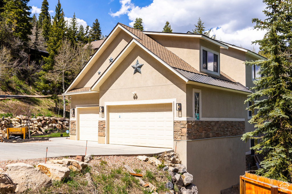 View of front of home featuring stucco siding, stone siding, concrete driveway, fence, and a garage