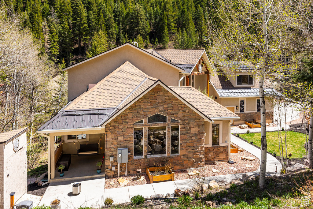 View of front of home with stone siding, a view of trees, stucco siding, roof with shingles, and a standing seam roof