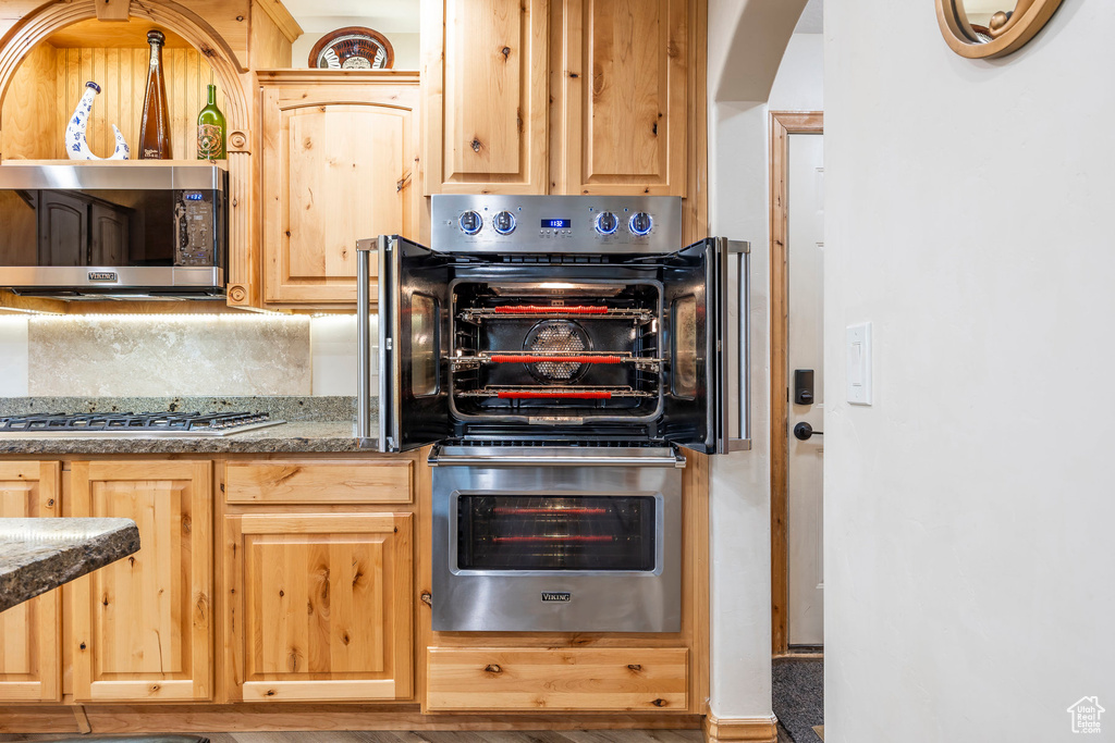 Kitchen featuring stainless steel appliances, arched walkways, light brown cabinetry, and dark stone counters
