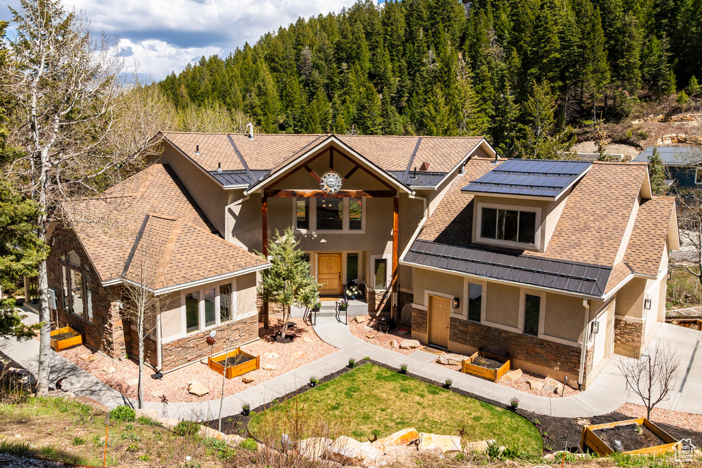 View of front of house with stone siding, stucco siding, solar panels, a view of trees, and driveway