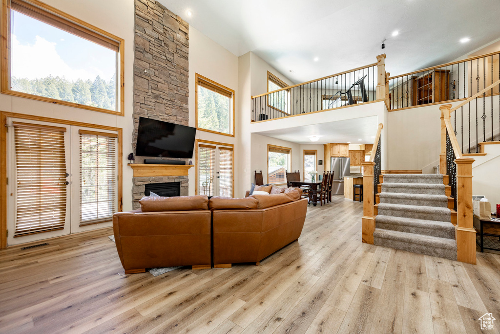 Living area featuring a towering ceiling, light wood-type flooring, stairs, a fireplace, and recessed lighting