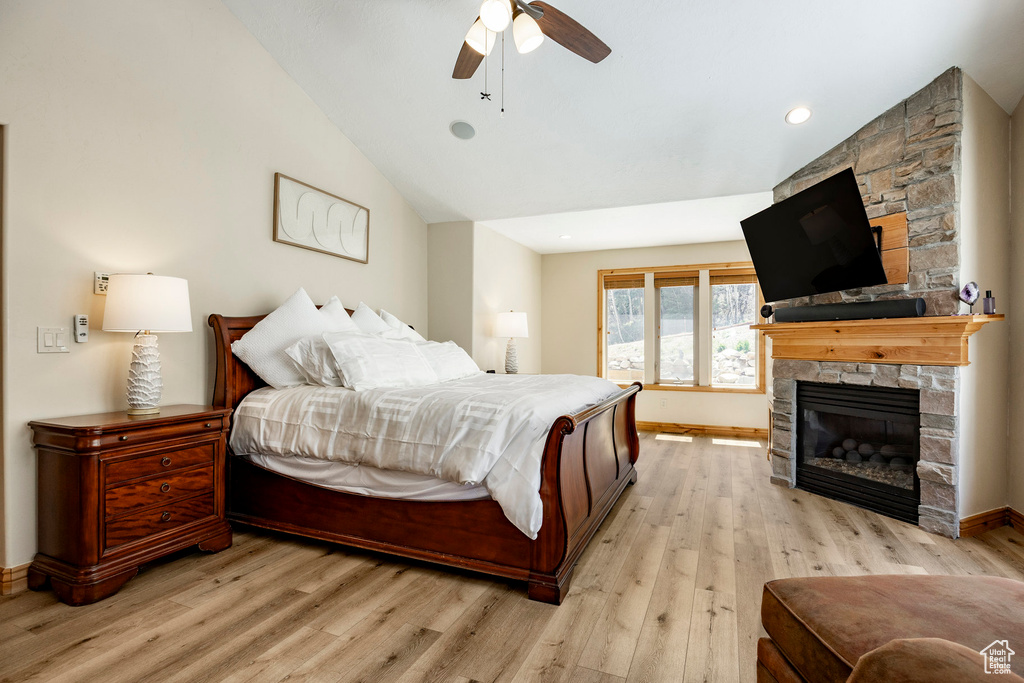 Bedroom featuring a stone fireplace, light wood finished floors, vaulted ceiling, baseboards, and a ceiling fan