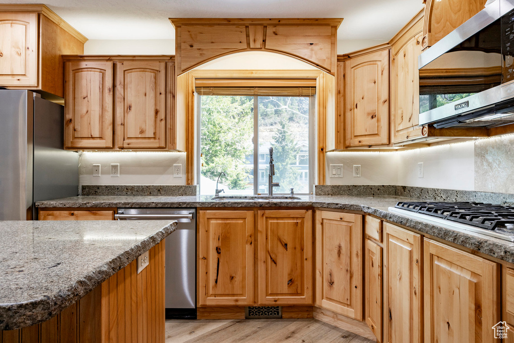 Kitchen featuring stainless steel appliances, a sink, light wood finished floors, dark stone counters, and light brown cabinets