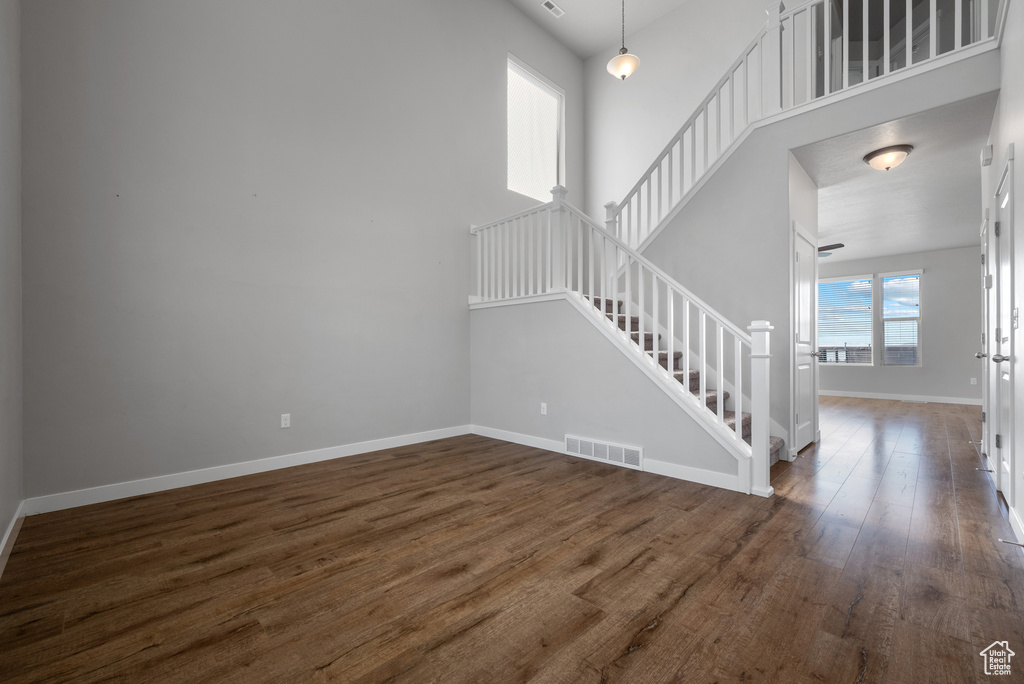 Unfurnished living room featuring stairs, wood finished floors, baseboards, and a high ceiling