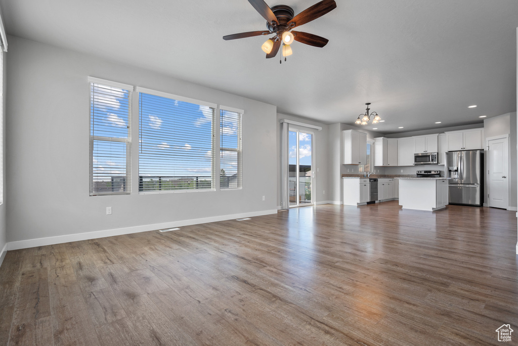 Unfurnished living room with a chandelier, recessed lighting, ceiling fan, baseboards, and dark wood-style flooring
