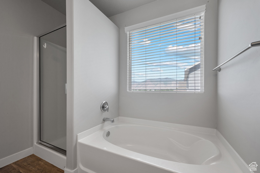 Bathroom with plenty of natural light, a garden tub, a stall shower, and wood finished floors