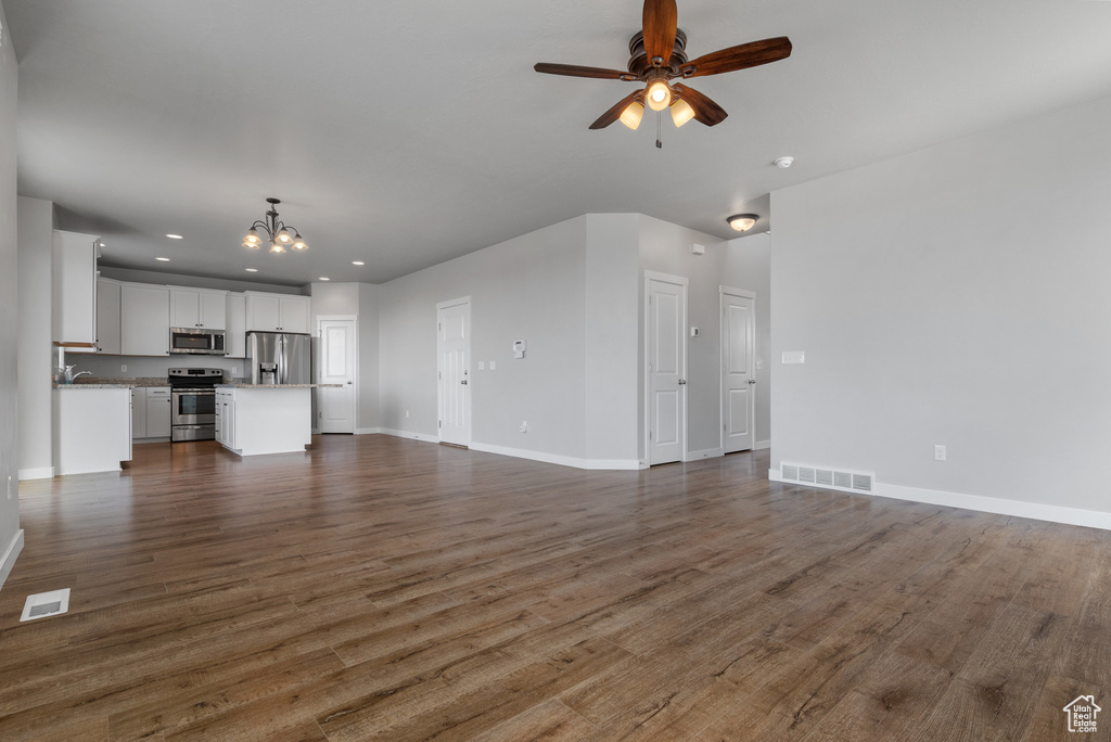 Unfurnished living room featuring a chandelier, ceiling fan, dark wood finished floors, baseboards, and recessed lighting