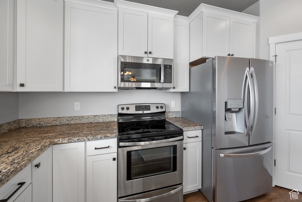 Kitchen featuring stainless steel appliances, white cabinets, and dark stone countertops