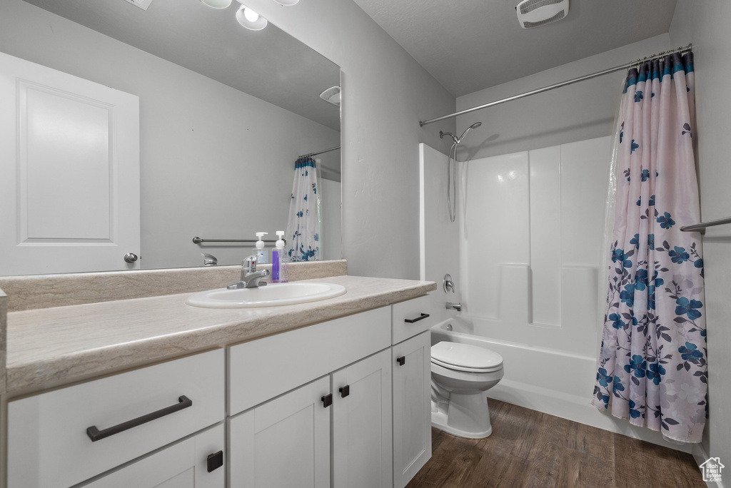 Bathroom with vanity, shower / tub combo, toilet, and wood finished floors