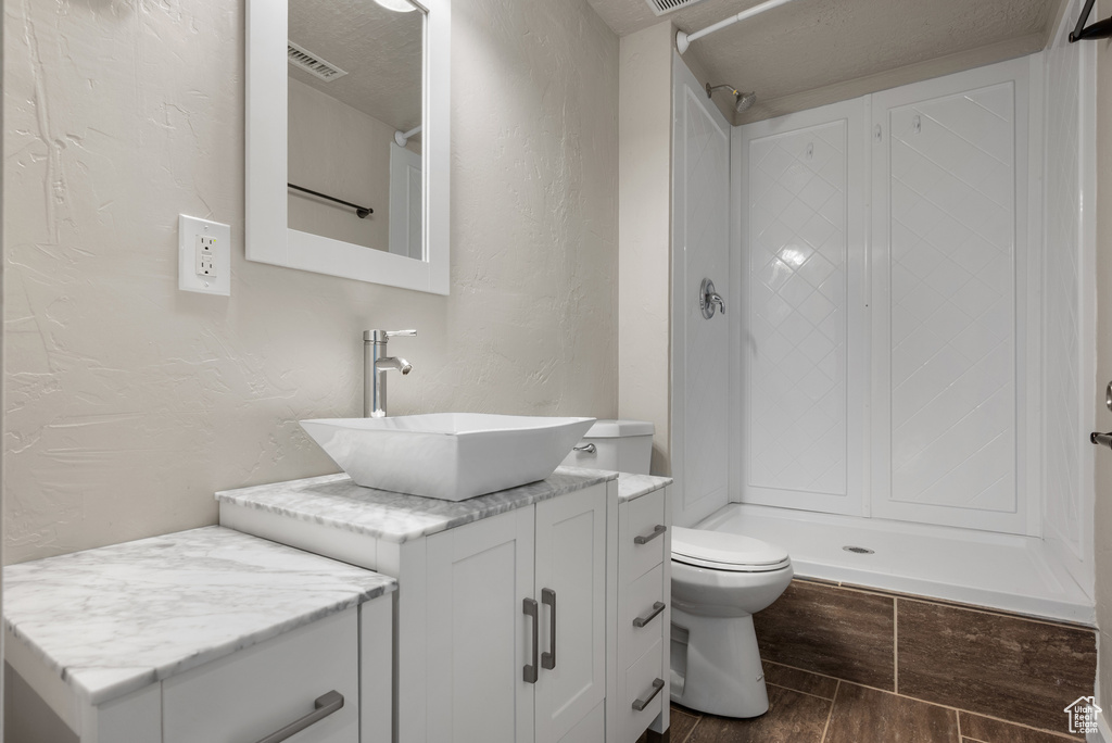 Bathroom featuring vanity, toilet, a textured wall, wood finished floors, and a shower