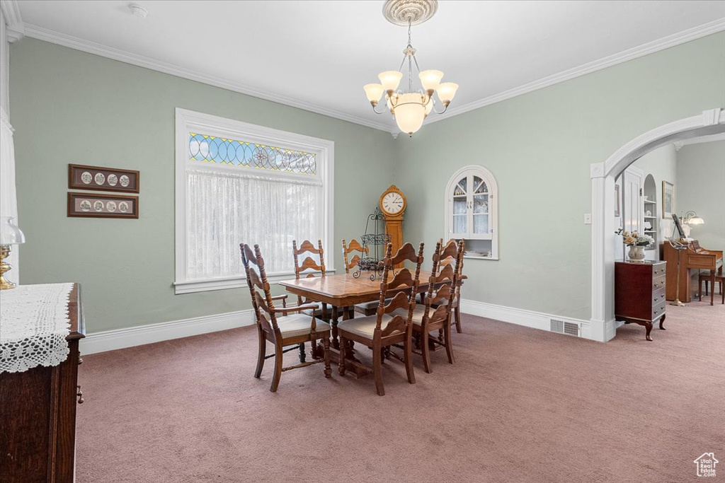 Carpeted dining area featuring ornamental molding and an inviting chandelier