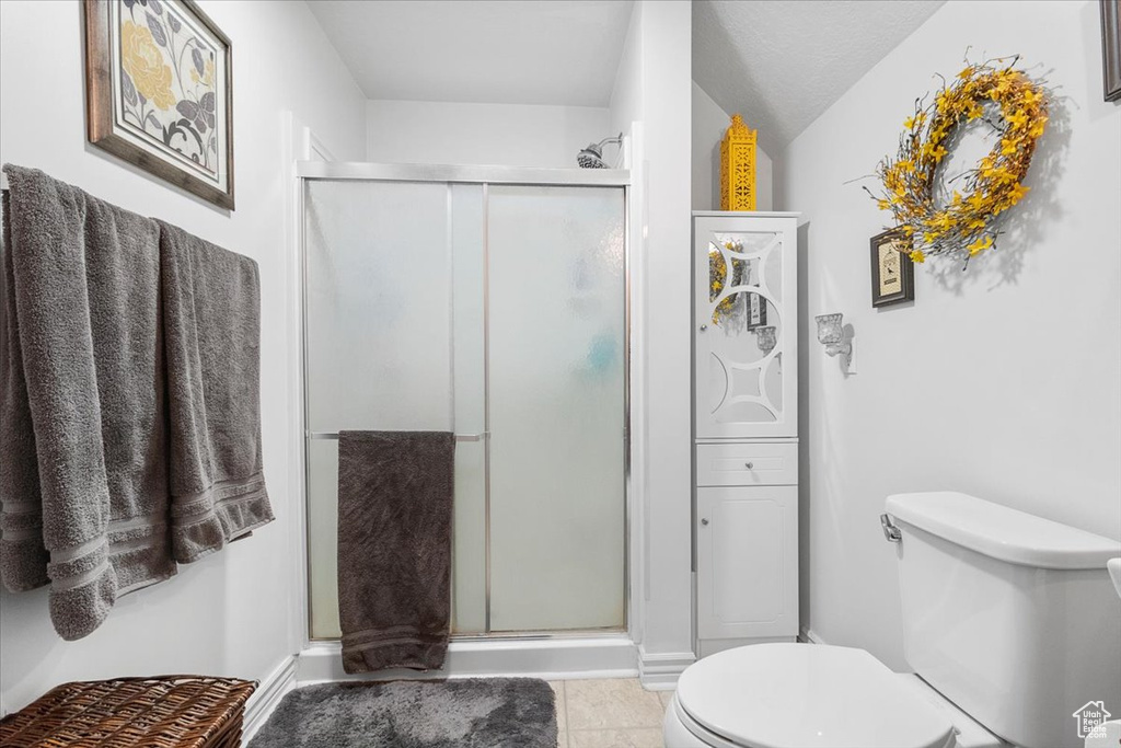 Bathroom with tile patterned flooring, toilet, a shower with shower door, and a textured ceiling