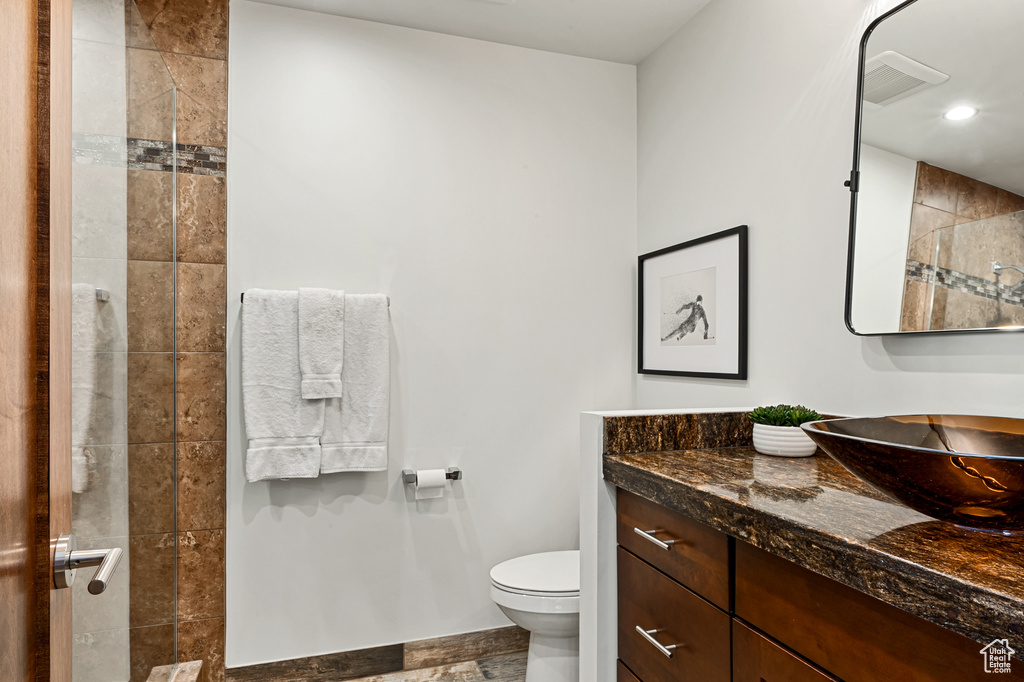 Full bathroom with toilet, recessed lighting, vanity, visible vents, and tiled shower