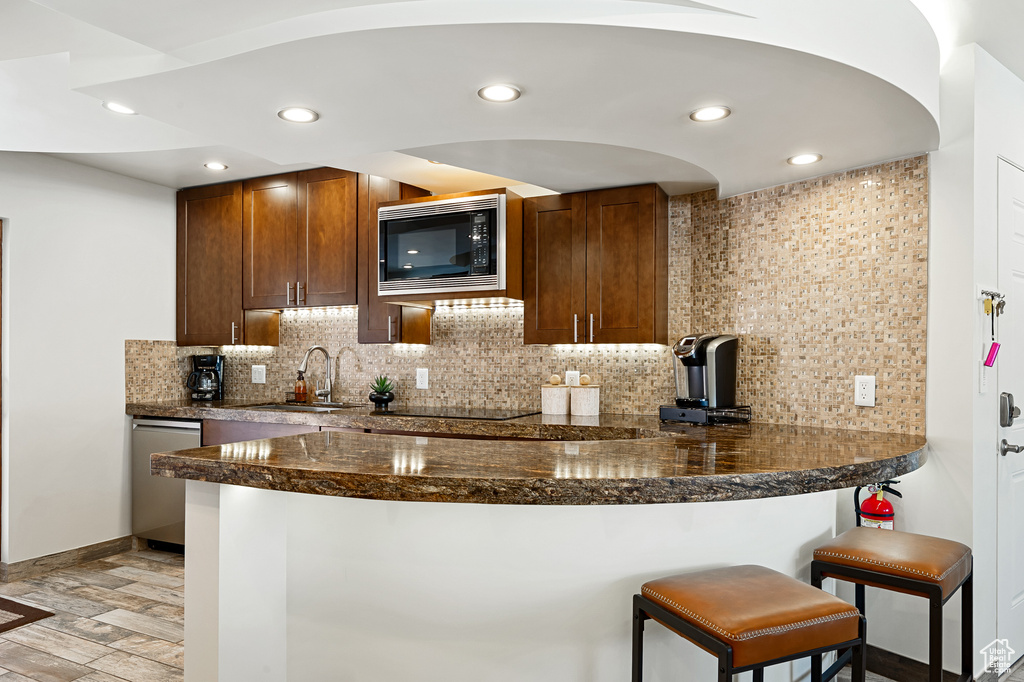 Kitchen with built in microwave, a sink, decorative backsplash, dishwasher, and dark countertops
