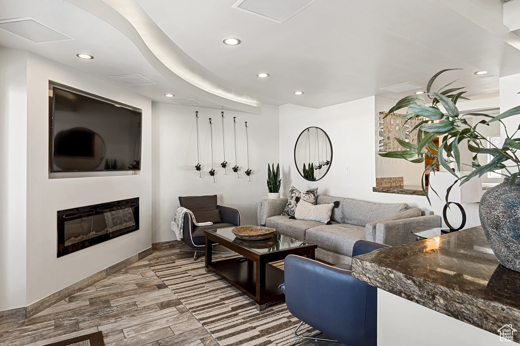 Living area with baseboards, wood finished floors, a glass covered fireplace, and recessed lighting