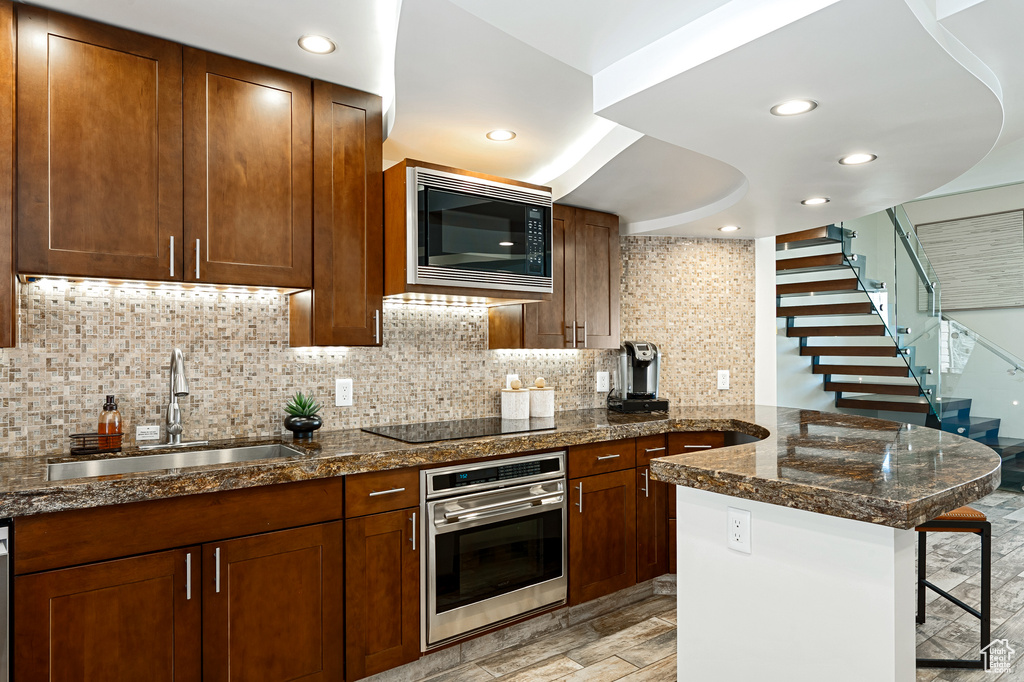 Kitchen with a breakfast bar area, backsplash, appliances with stainless steel finishes, a sink, and a peninsula