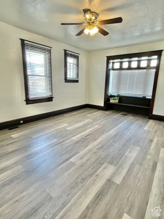 Unfurnished room with ceiling fan, light wood-type flooring, and a textured ceiling